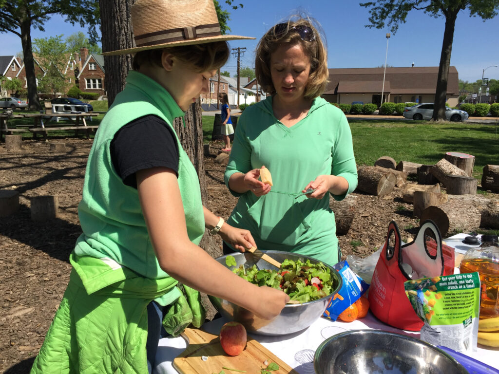 First grader at Mallinckdrodt Academy preparing salad with the help from Amanda Doyle a parent of a 2nd grader at Mallinckrodt.