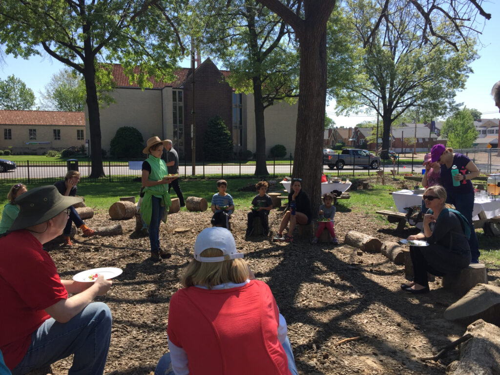 GGI staff and board members, Mallinckdot parents, and students sitting down at school's outdoor classroom at the end of the work day to share a salad made using ingredients from the garden.